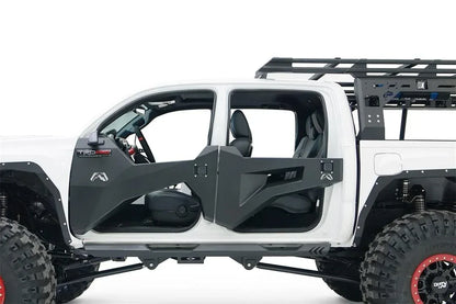 Fab Fours trail doors on a white Toyota Tacoma, driver-side close-up, showing the open-top faceted steel front and rear doors with the Fab Fours logo and paddle latches