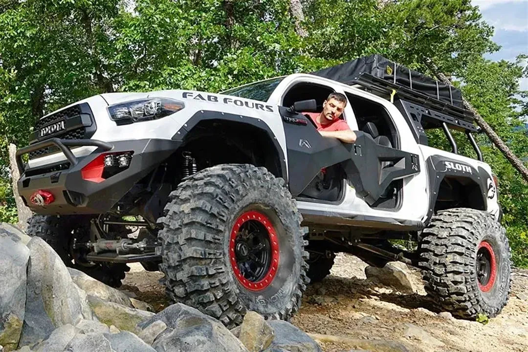 Fab Fours trail doors on a lifted white Toyota Tacoma crawling over rocks, front driver-side view, showing the open-top doors with a Fab Fours front bumper and fenders