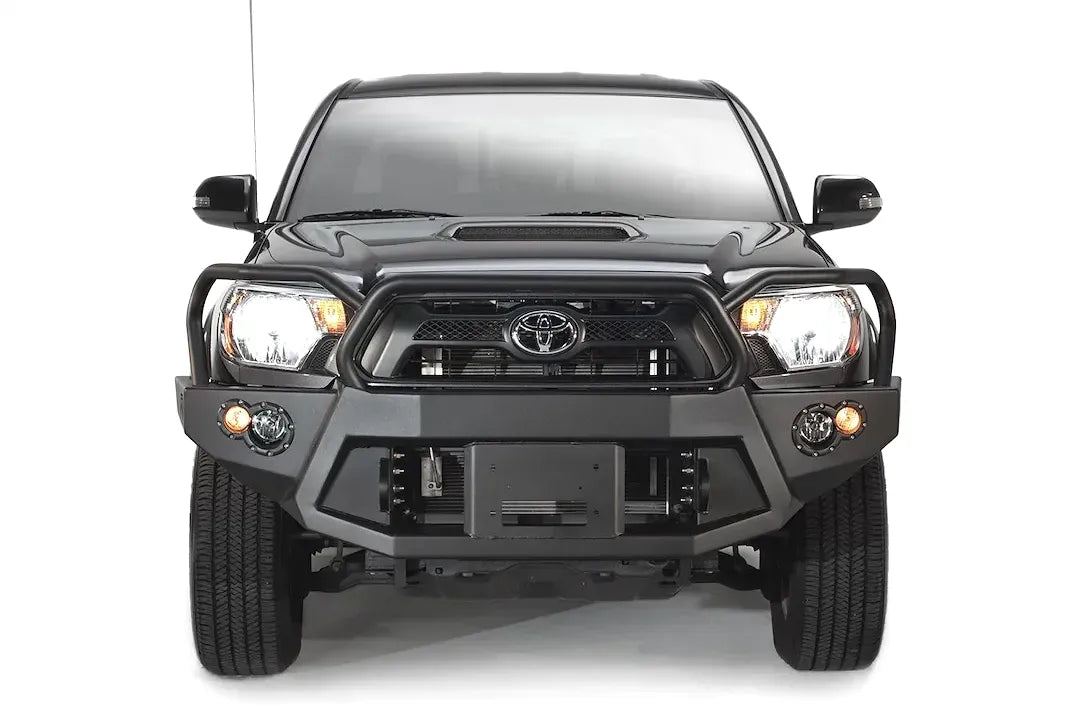 Fab Fours Premium front bumper with full guard on a black Toyota Tacoma, front view, showing the full grille guard, recessed winch plate and round fog lights