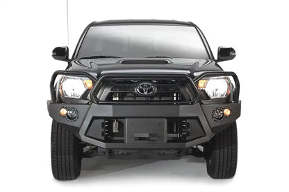 Fab Fours Premium front bumper with full guard on a black Toyota Tacoma, front view, showing the full grille guard, recessed winch plate and round fog lights