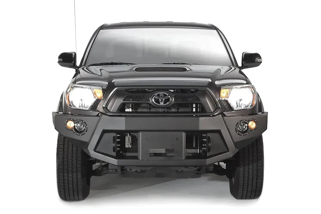 Fab Fours Premium front bumper on a black Toyota Tacoma, front view, showing the recessed winch plate, round fog lights and angled end caps