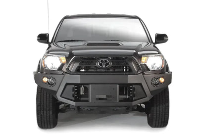 Fab Fours Premium front bumper on a black Toyota Tacoma, front view, showing the recessed winch plate, round fog lights and angled end caps