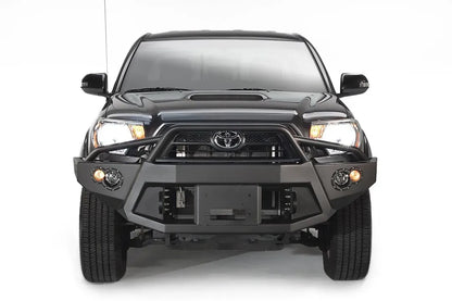 Fab Fours Premium front bumper with pre-runner guard on a black Toyota Tacoma, front view, showing the pre-runner hoop, recessed winch plate and round fog lights