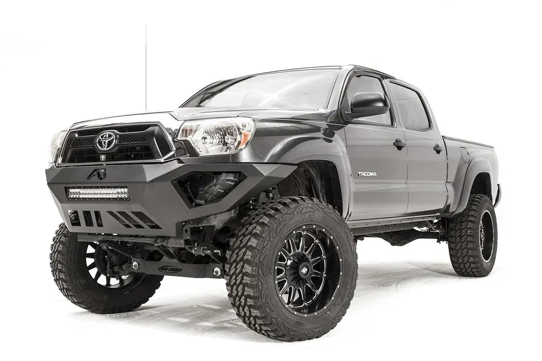 Fab Fours Vengeance front bumper on a gray Toyota Tacoma, front three-quarter view from the driver side, showing the LED light bar, angled end caps and skid plate