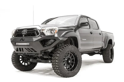 Fab Fours Vengeance front bumper on a gray Toyota Tacoma, front three-quarter view from the driver side, showing the LED light bar, angled end caps and skid plate