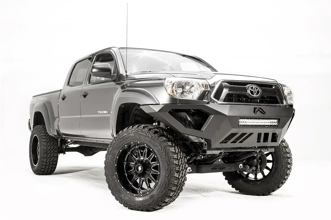 Fab Fours Vengeance front bumper on a gray Toyota Tacoma, front three-quarter view from the passenger side, showing the LED light bar, angled end caps and skid plate