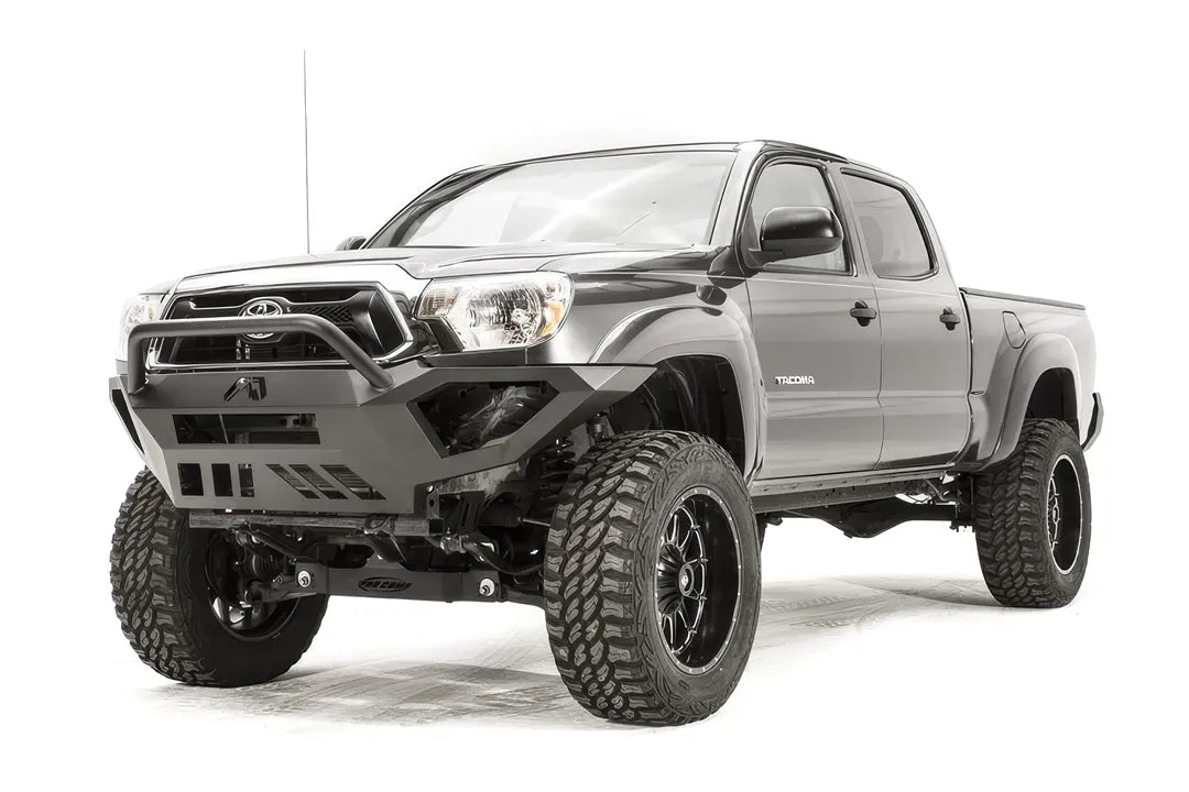 Fab Fours Vengeance front bumper with high pre-runner guard on a gray Toyota Tacoma, front three-quarter view from the driver side, showing the high pre-runner hoop, angled end caps and skid plate