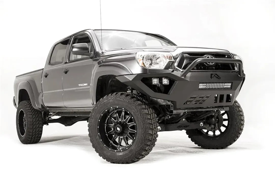 Fab Fours Vengeance front bumper with high pre-runner guard on a gray Toyota Tacoma, front three-quarter view from the passenger side, showing the high pre-runner hoop, LED light bar and cube lights