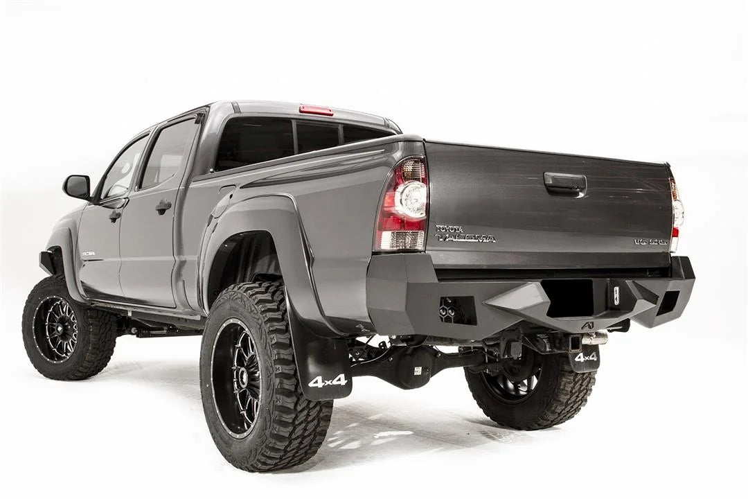 Fab Fours Vengeance rear bumper on a gray Toyota Tacoma, rear three-quarter view from the driver side, showing the angled end caps, light cutouts and receiver hitch