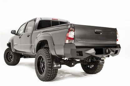 Fab Fours Vengeance rear bumper on a gray Toyota Tacoma, rear three-quarter view from the driver side, showing the angled end caps, light cutouts and receiver hitch