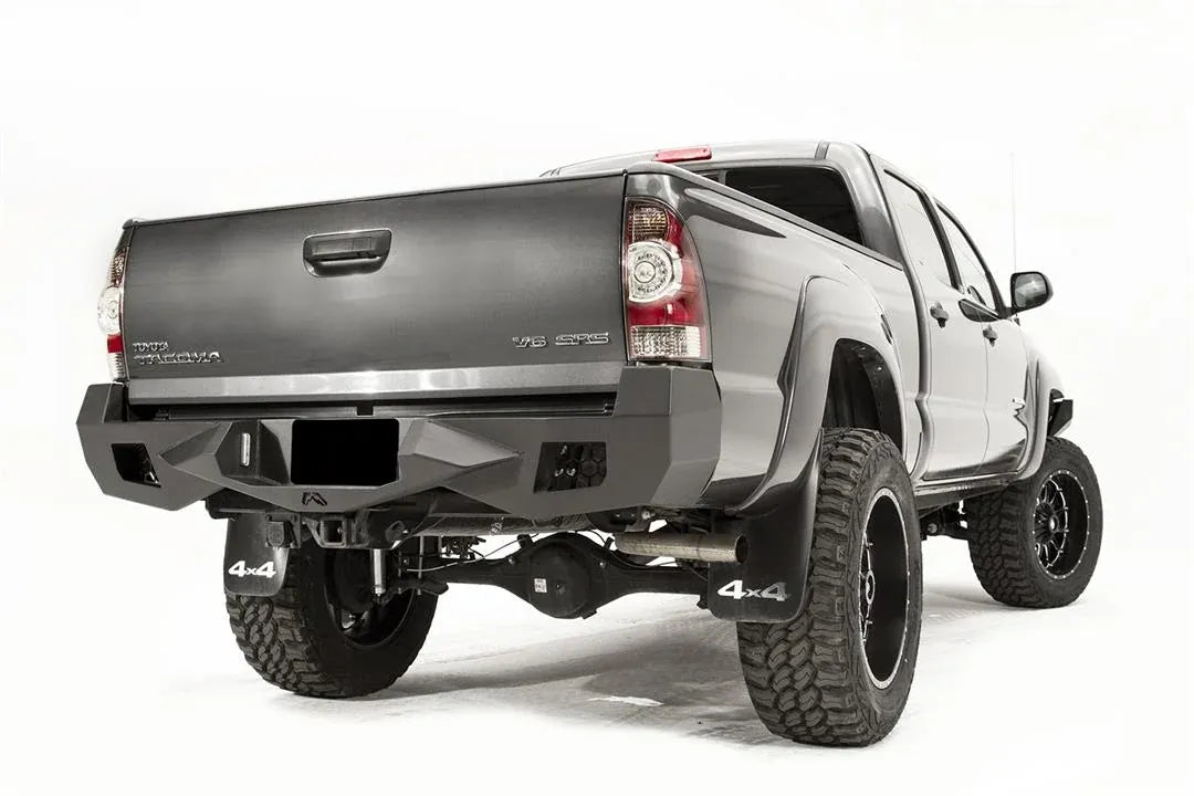 Fab Fours Vengeance rear bumper on a gray Toyota Tacoma, rear three-quarter view from the passenger side, showing the honeycomb light cutouts, plate recess and angled end caps