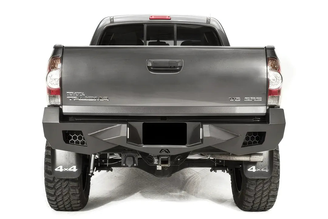 Fab Fours Vengeance rear bumper on a gray Toyota Tacoma, straight-on rear view, showing the honeycomb light cutouts, centre plate recess and receiver hitch