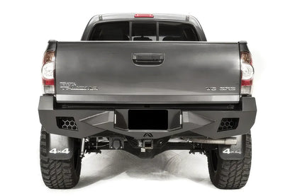 Fab Fours Vengeance rear bumper on a gray Toyota Tacoma, straight-on rear view, showing the honeycomb light cutouts, centre plate recess and receiver hitch