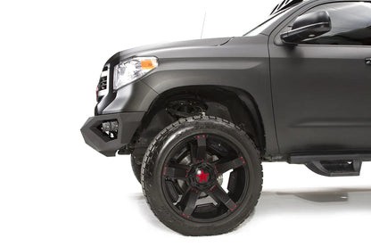 Fab Fours Vengeance front bumper on a matte black Toyota Tundra, close-up of the front corner from the driver side, showing the angled bumper end and wheel clearance