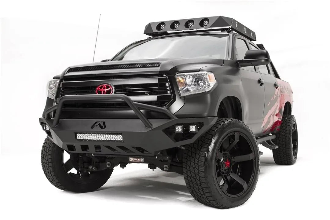 Fab Fours Vengeance front bumper with pre-runner guard on a matte black Toyota Tundra, front three-quarter view from the driver side, showing the pre-runner hoop, LED light bar and cube lights