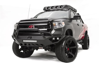 Fab Fours Vengeance front bumper with pre-runner guard on a matte black Toyota Tundra, front three-quarter view from the driver side, showing the pre-runner hoop, LED light bar and cube lights