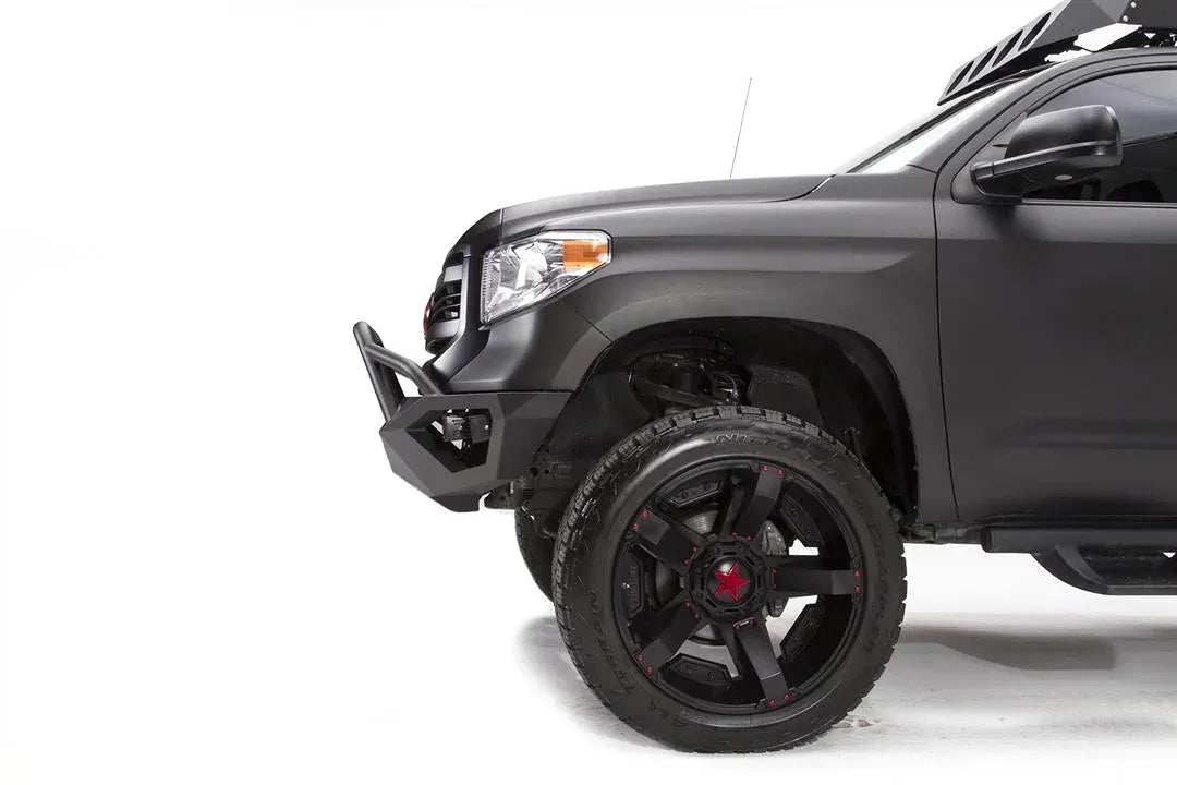Fab Fours Vengeance front bumper with pre-runner guard on a matte black Toyota Tundra, close-up of the front corner from the driver side, showing the pre-runner tube, angled bumper end and wheel clearance