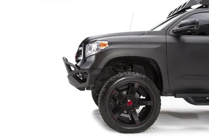 Fab Fours Vengeance front bumper with pre-runner guard on a matte black Toyota Tundra, close-up of the front corner from the driver side, showing the pre-runner tube, angled bumper end and wheel clearance
