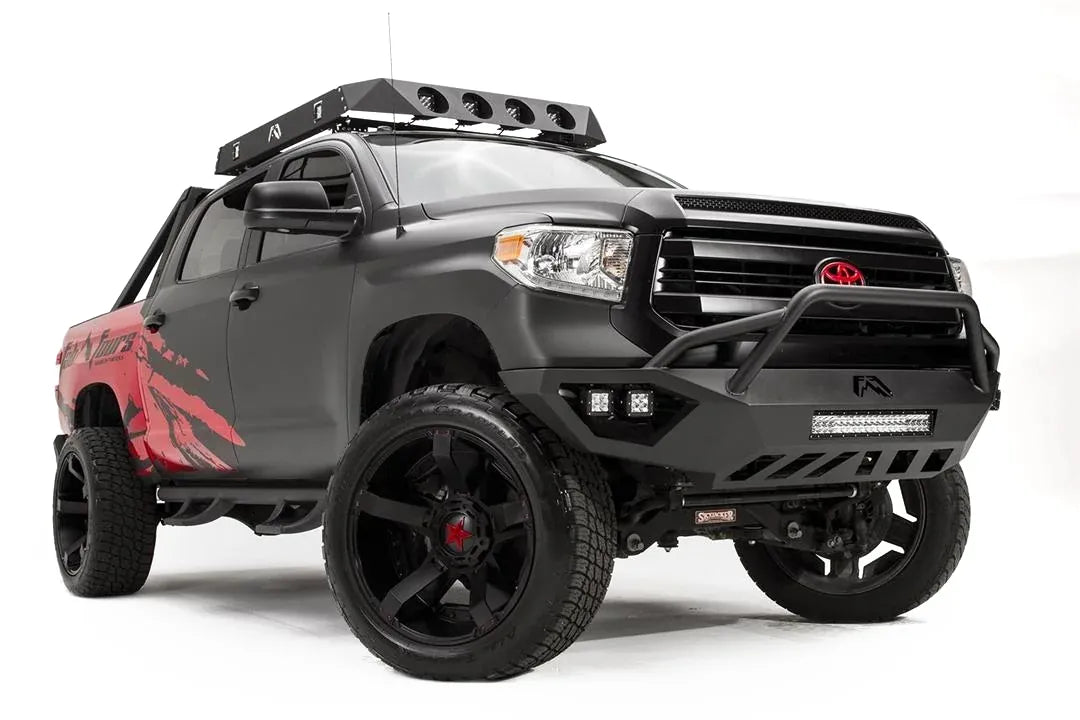 Fab Fours Vengeance front bumper with pre-runner guard on a matte black Toyota Tundra, front three-quarter view from the passenger side, showing the pre-runner hoop, LED light bar and cube lights