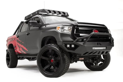 Fab Fours Vengeance front bumper with pre-runner guard on a matte black Toyota Tundra, front three-quarter view from the passenger side, showing the pre-runner hoop, LED light bar and cube lights