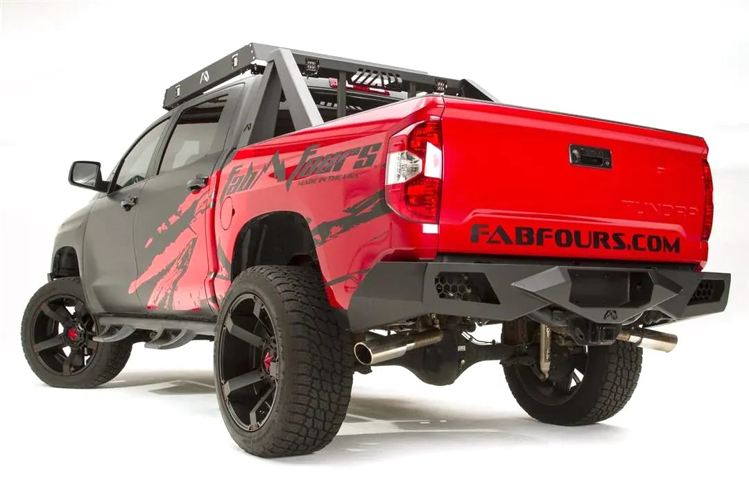 Fab Fours Vengeance rear bumper on a red and black Toyota Tundra, opposite rear three-quarter view, showing the angular end caps, light pods, and center hitch opening