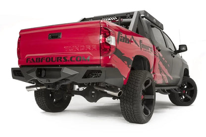 Fab Fours Vengeance rear bumper on a red and black Toyota Tundra, rear three-quarter view, showing the bumper corners, recessed light pods, and dual exhaust tips