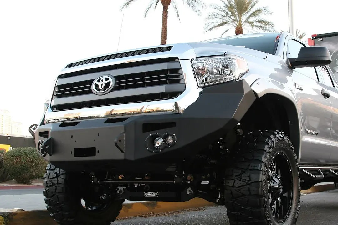 Fab Fours Premium front bumper on a silver Toyota Tundra, front three-quarter view outdoors, showing the winch-ready center section, round fog lights, and wraparound end caps