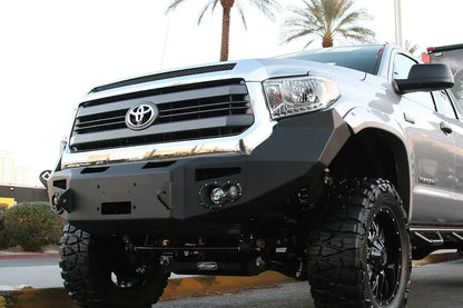 Fab Fours Premium front bumper on a silver Toyota Tundra, front three-quarter view outdoors, showing the winch-ready center section, round fog lights, and wraparound end caps