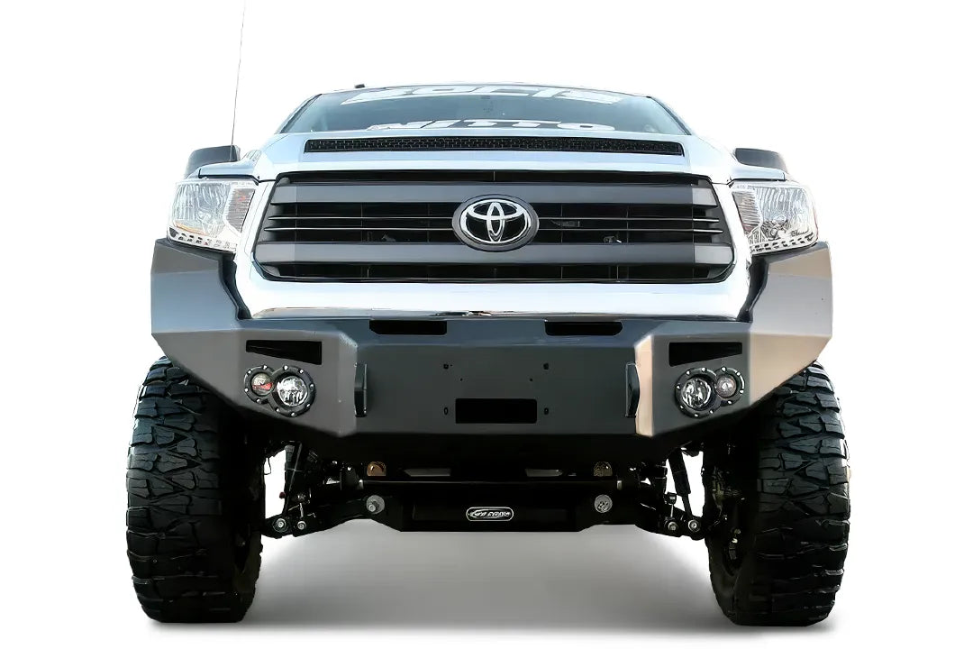 Fab Fours Premium front bumper on a silver Toyota Tundra, straight-on front view outdoors, showing the full-width bumper, round fog lights, and winch mount opening