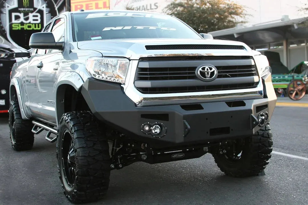 Fab Fours Premium front bumper on a silver Toyota Tundra, front three-quarter view outdoors, showing the no-guard design, round fog lights, and winch fairlead opening