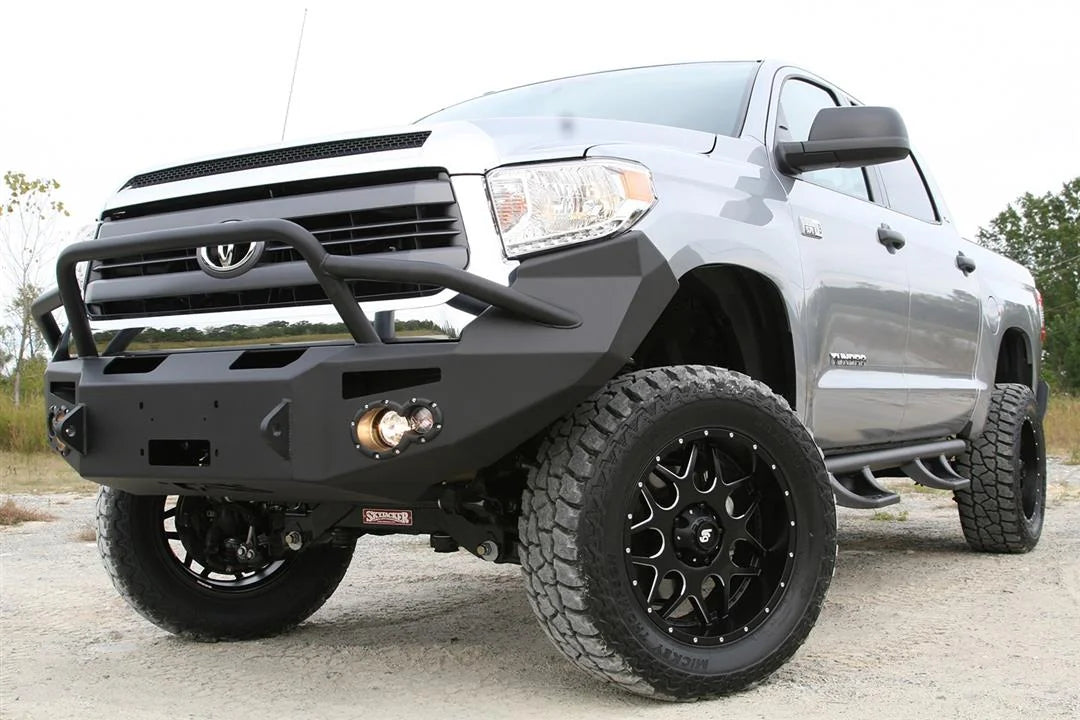 Fab Fours Premium front bumper with pre-runner guard on a silver Toyota Tundra, low front three-quarter view outdoors, showing the pre-runner hoop, fog light, and wraparound end cap