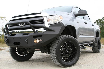 Fab Fours Premium front bumper with pre-runner guard on a silver Toyota Tundra, low front three-quarter view outdoors, showing the pre-runner hoop, fog light, and wraparound end cap