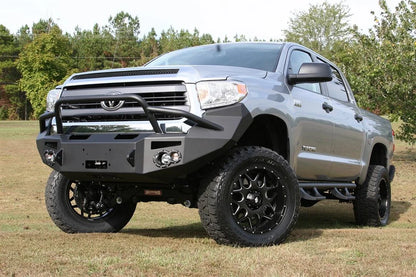 Fab Fours Premium front bumper with pre-runner guard on a silver Toyota Tundra, front three-quarter view outdoors, showing the pre-runner hoop, round fog lights, and winch-ready center section