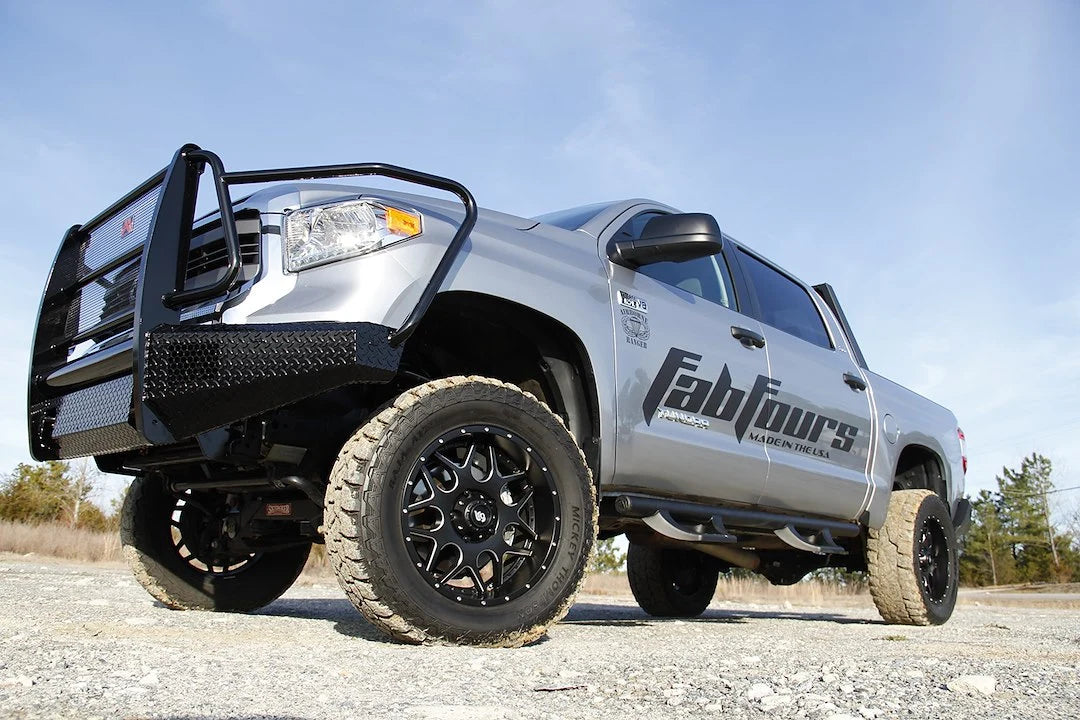 Fab Fours Black Steel front bumper with full guard on a silver Toyota Tundra, low front three-quarter view outdoors, showing the full grille guard, diamond-plate face, and side wings