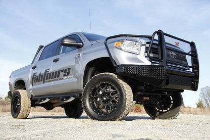 Fab Fours Black Steel front bumper with full guard on a silver Toyota Tundra, low front three-quarter view outdoors, showing the full grille guard, diamond-plate face, and headlight hoops