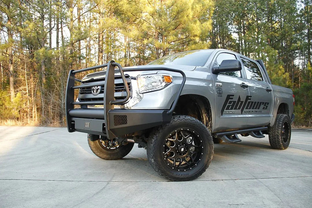 Fab Fours Black Steel Elite front bumper with full guard on a silver Toyota Tundra, front three-quarter view outdoors, showing the full grille guard, headlight hoops, and mesh light openings