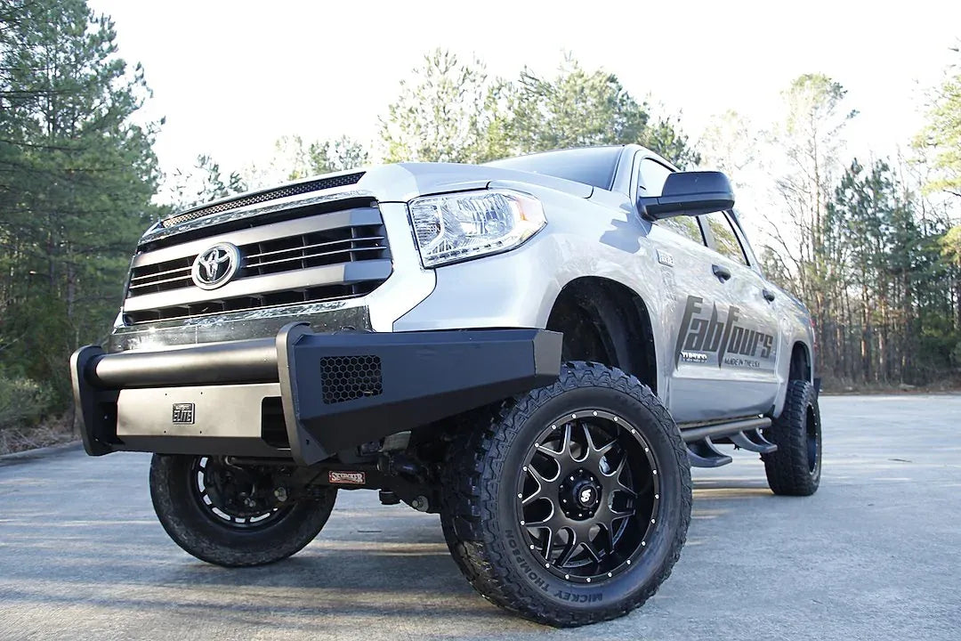 Fab Fours Black Steel Elite front bumper on a silver Toyota Tundra, low front three-quarter view outdoors, showing the no-guard design, mesh light opening, and Elite badge