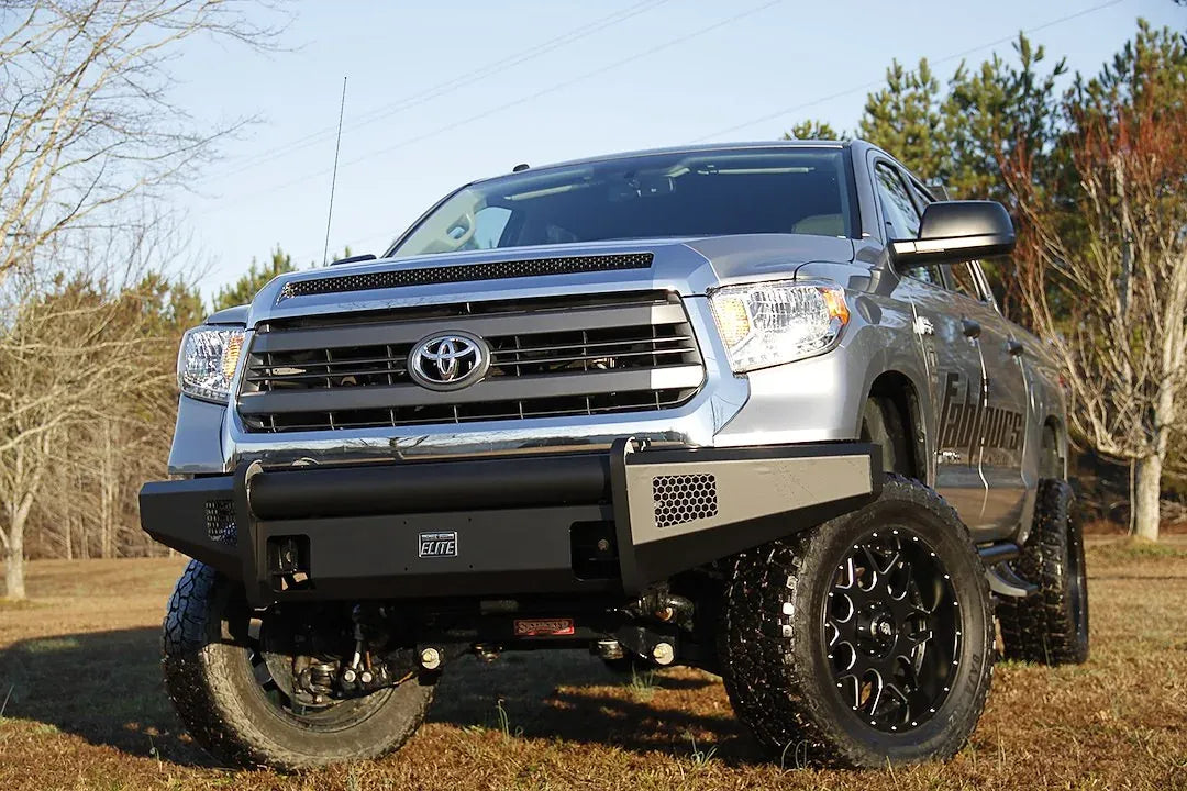 Fab Fours Black Steel Elite front bumper on a silver Toyota Tundra, front view outdoors, showing the no-guard design, Elite badge, and mesh light openings