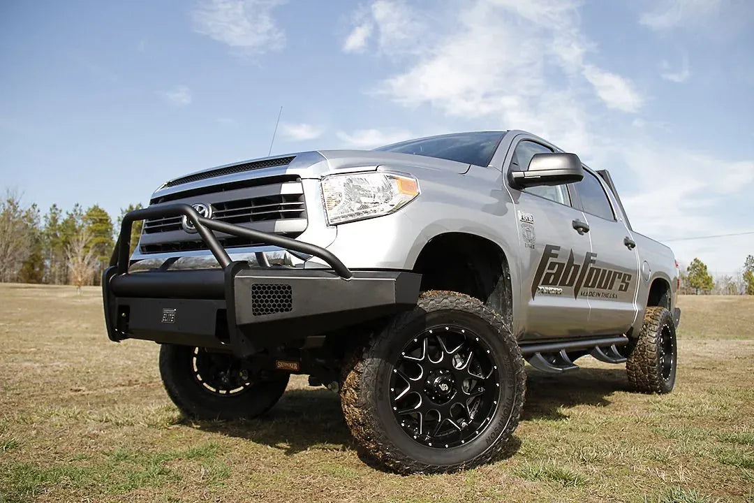 Fab Fours Black Steel Elite front bumper with pre-runner guard on a silver Toyota Tundra, wider front three-quarter view outdoors, showing the pre-runner hoop, Elite badge, and mesh light opening