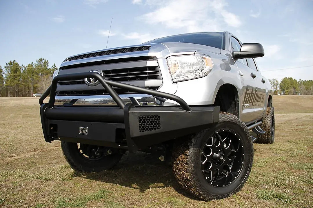 Fab Fours Black Steel Elite front bumper with pre-runner guard on a silver Toyota Tundra, front three-quarter view outdoors, showing the pre-runner hoop, mesh light opening, and wraparound end cap