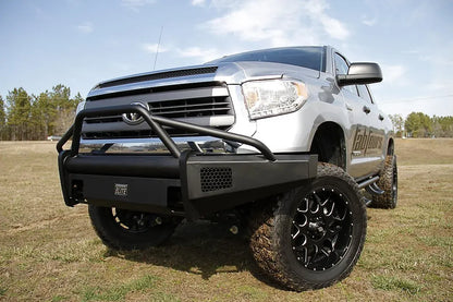 Fab Fours Black Steel Elite front bumper with pre-runner guard on a silver Toyota Tundra, front three-quarter view outdoors, showing the pre-runner hoop, mesh light opening, and wraparound end cap
