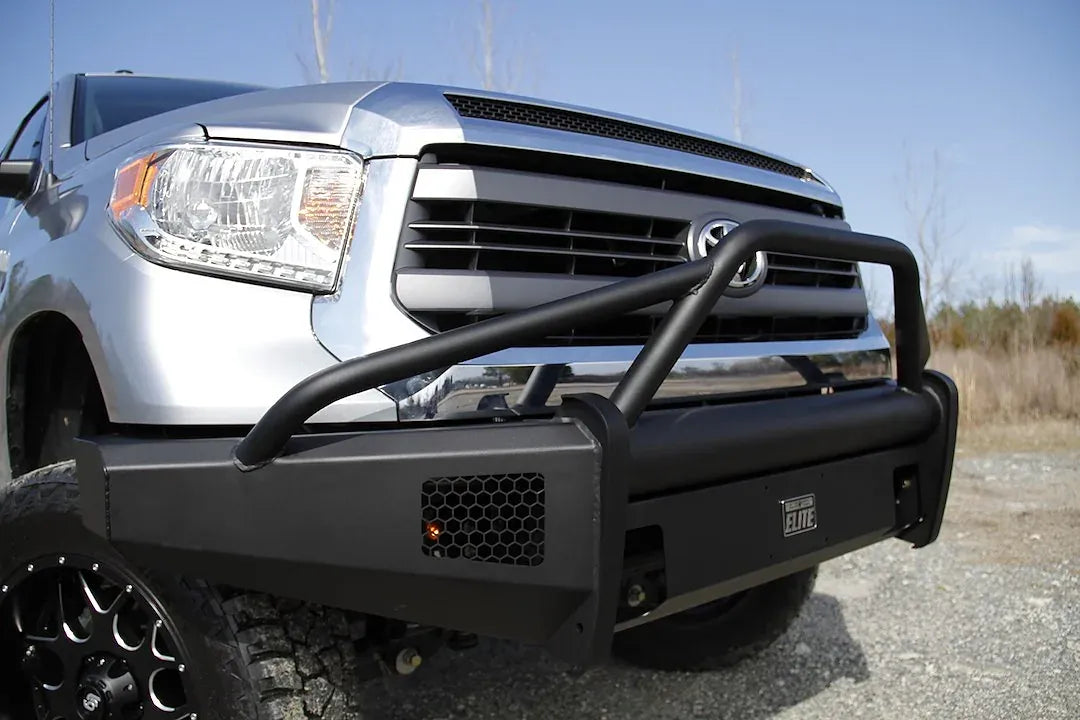 Fab Fours Black Steel Elite front bumper with pre-runner guard on a silver Toyota Tundra, close front three-quarter view outdoors, showing the pre-runner hoop, mesh light opening, and Elite badge