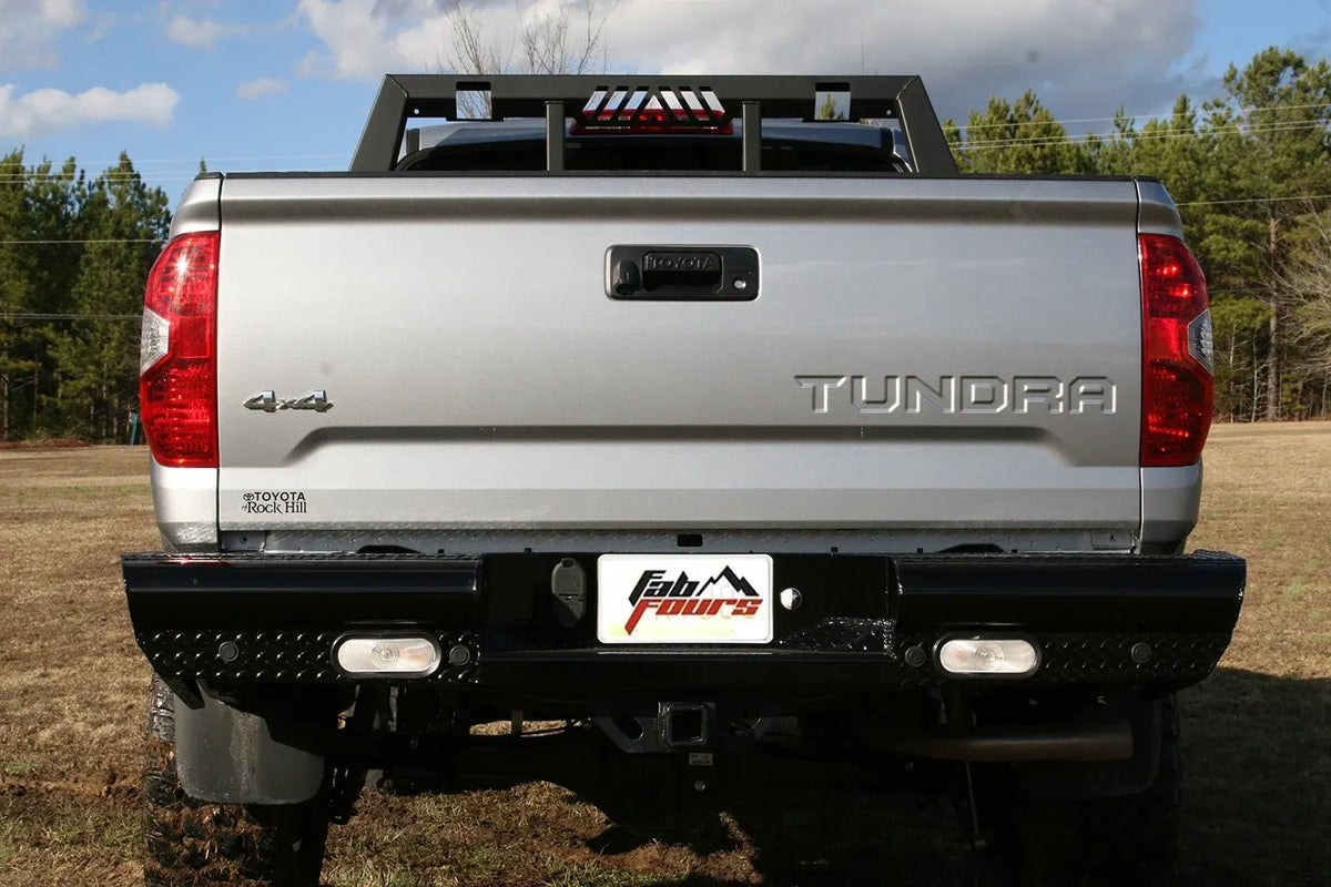 Fab Fours Black Steel rear bumper on a silver Toyota Tundra, straight-on rear view outdoors, showing the diamond-plate face, recessed lights, and center plate mount