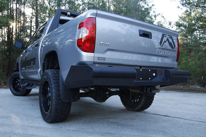 Fab Fours Black Steel Elite rear bumper on a silver Toyota Tundra, low rear three-quarter view outdoors, showing the angled end cap, center plate mount, and receiver hitch