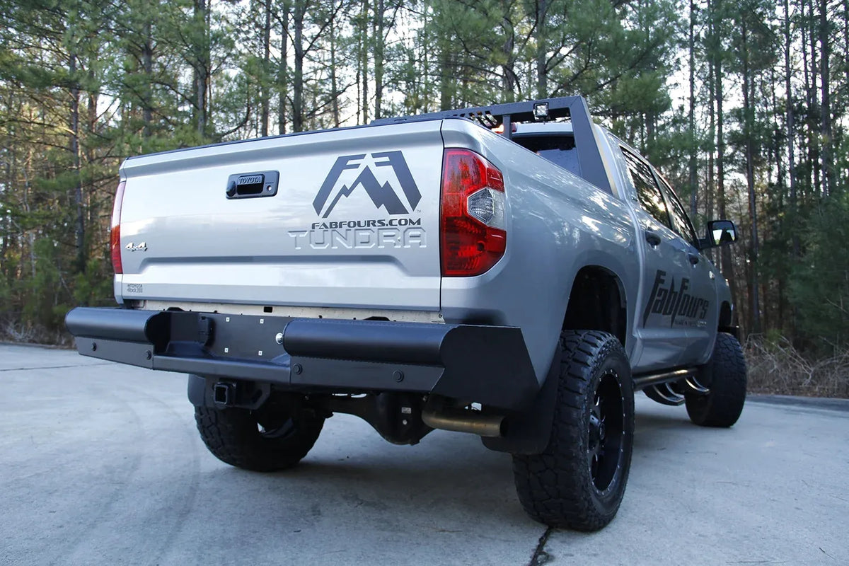 Fab Fours Black Steel Elite rear bumper on a silver Toyota Tundra, low rear three-quarter view outdoors, showing the smooth steel face, angled end caps, and receiver hitch