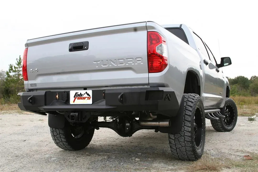 Fab Fours Premium rear bumper on a silver Toyota Tundra, rear three-quarter view outdoors, showing the recessed light pods, center plate mount, and receiver hitch