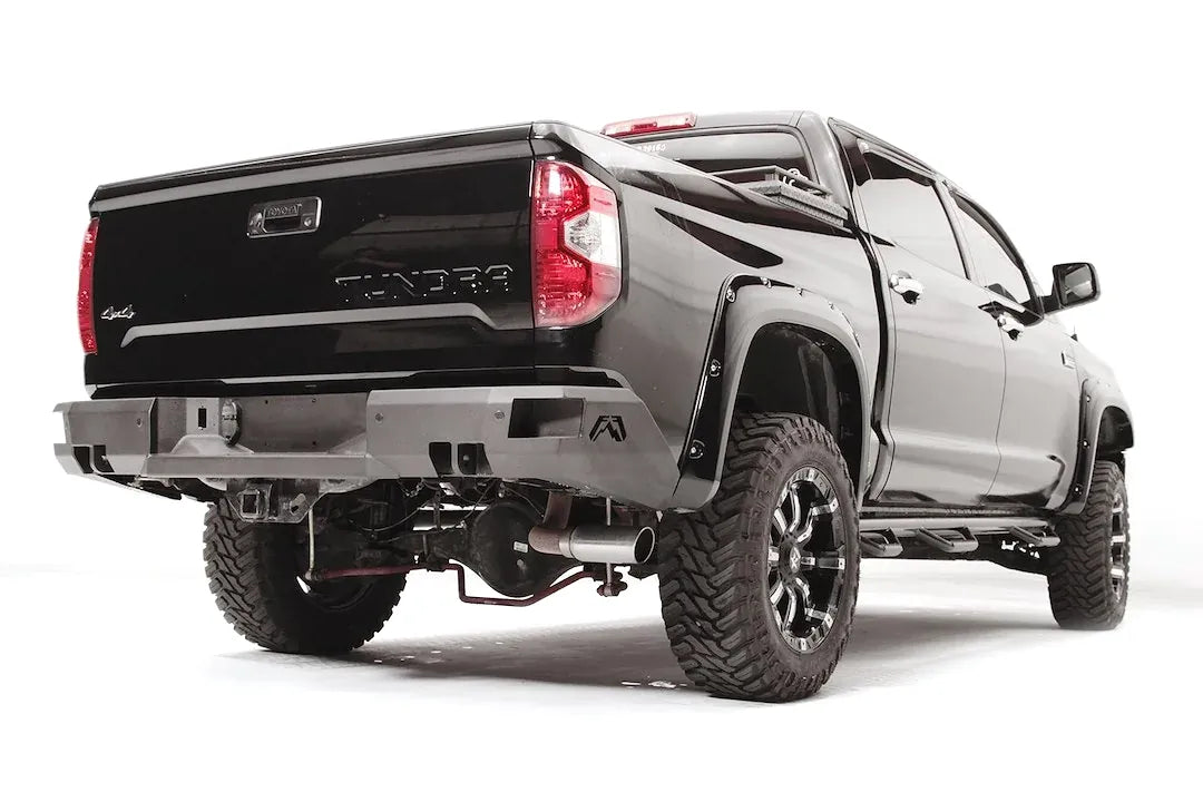 Fab Fours Premium rear bumper on a black Toyota Tundra, rear three-quarter view, showing the angular end caps, center plate mount, and receiver hitch