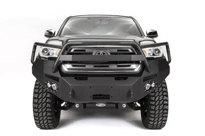 Fab Fours Premium front bumper with pre-runner guard on a dark gray Toyota Tacoma, straight-on front view, showing the guard hoop, round fog lights, and winch mount plate