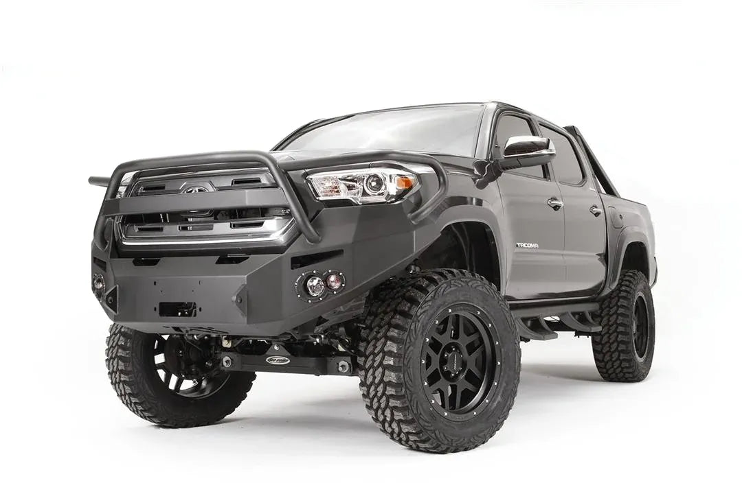 Fab Fours Premium front bumper with pre-runner guard on a dark gray Toyota Tacoma, front three-quarter view, showing the guard hoop, round fog lights, and wraparound end caps