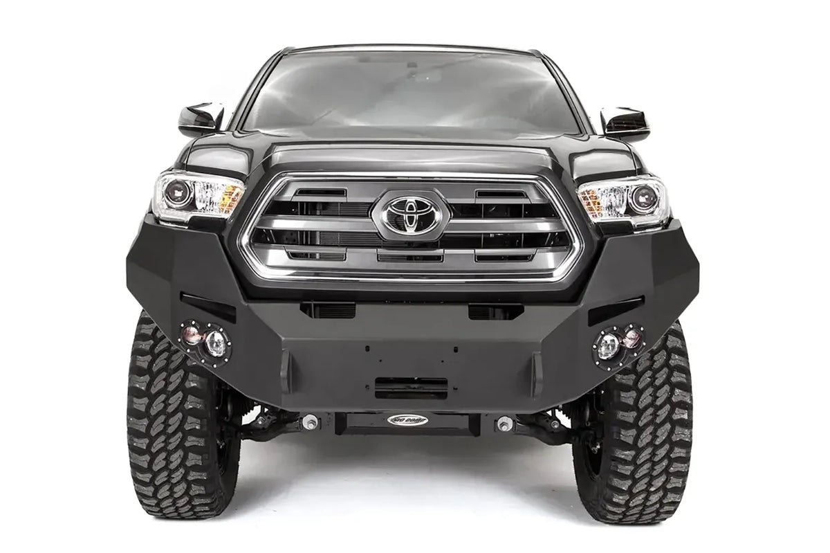 Fab Fours Premium front bumper on a dark gray Toyota Tacoma, straight-on front view, showing the full-width bumper, round fog lights, and winch mount plate